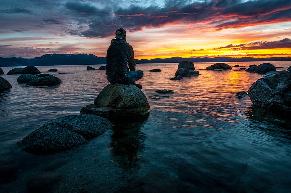 A serene person meditating with arms stretched wide towards a warm sunset.
